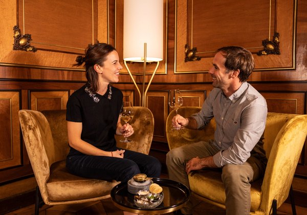 Ein Paar sitzt in bequemen Sesseln und stößt in einer eleganten Lounge auf den Abend an.