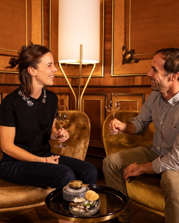 Ein Paar sitzt in bequemen Sesseln und stößt in einer eleganten Lounge auf den Abend an.