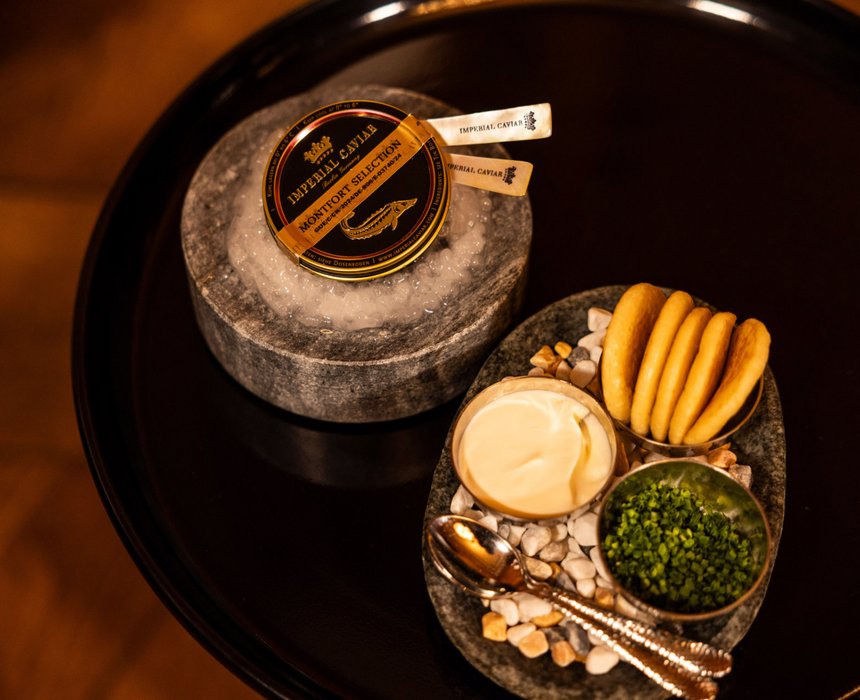 Ein Arrangement mit Imperial Caviar, serviert mit feiner Creme, Schnittlauch und Crackern auf einem eleganten Teller.