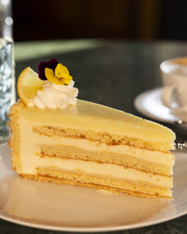 Ein Stück Zitronencreme-Torte auf einem Teller mit einer Tasse Kaffee im Hintergrund, perfekt für eine gemütliche Kaffeepause.