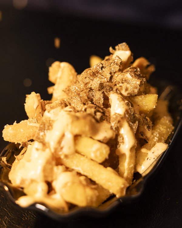 Eine Portion knuspriger Pommes, verfeinert mit Trüffelraspeln und cremigem Saucen-Topping, auf einem dunklen Hintergrund serviert.