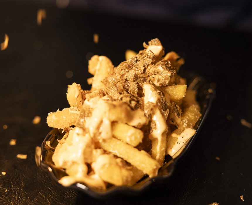 Eine Portion knuspriger Pommes, verfeinert mit Trüffelraspeln und cremigem Saucen-Topping, auf einem dunklen Hintergrund serviert.