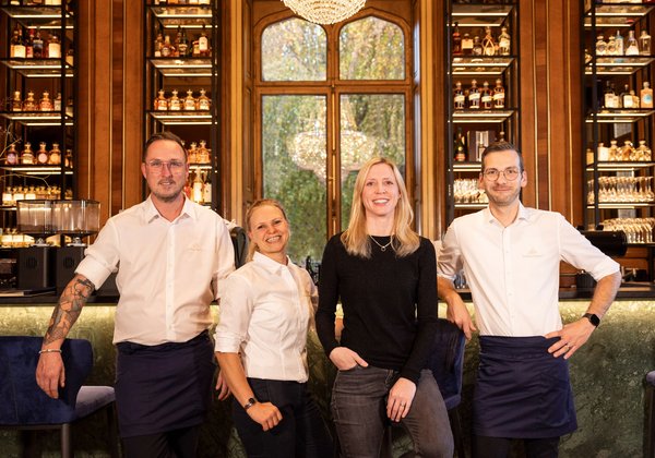 Das Team der Bar im Schloss Montfort – Mitarbeiter und Leitung vor einem Regal mit Spirituosen und Weingläsern.