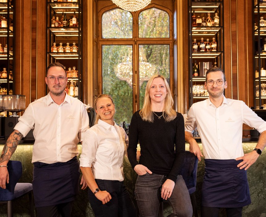 Das Team der Bar im Schloss Montfort – Mitarbeiter und Leitung vor einem Regal mit Spirituosen und Weingläsern.