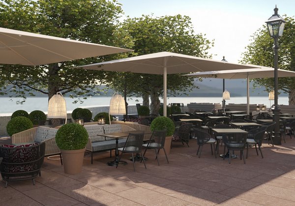 Die Terrasse des Schloss Montfort mit eingedeckten Tischen, Bäumen und Sonnenschirmen